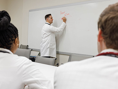 Instructor writing thw words heart failure on a white board as two students look on.